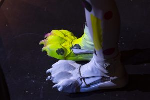 Two shoes have leopard toes with claws attached to the toe cap. One shoe is all white, the other is neon yellow with pink claws and black polka dots.